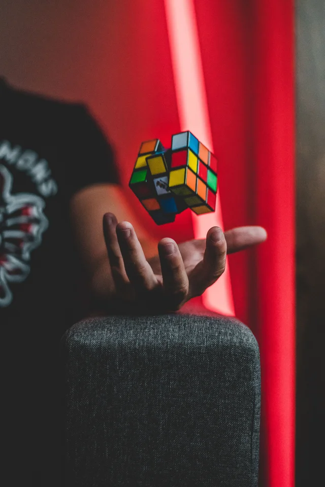 A scrambled Rubik's cube tumbling above an open hand in a dark red-lit room.