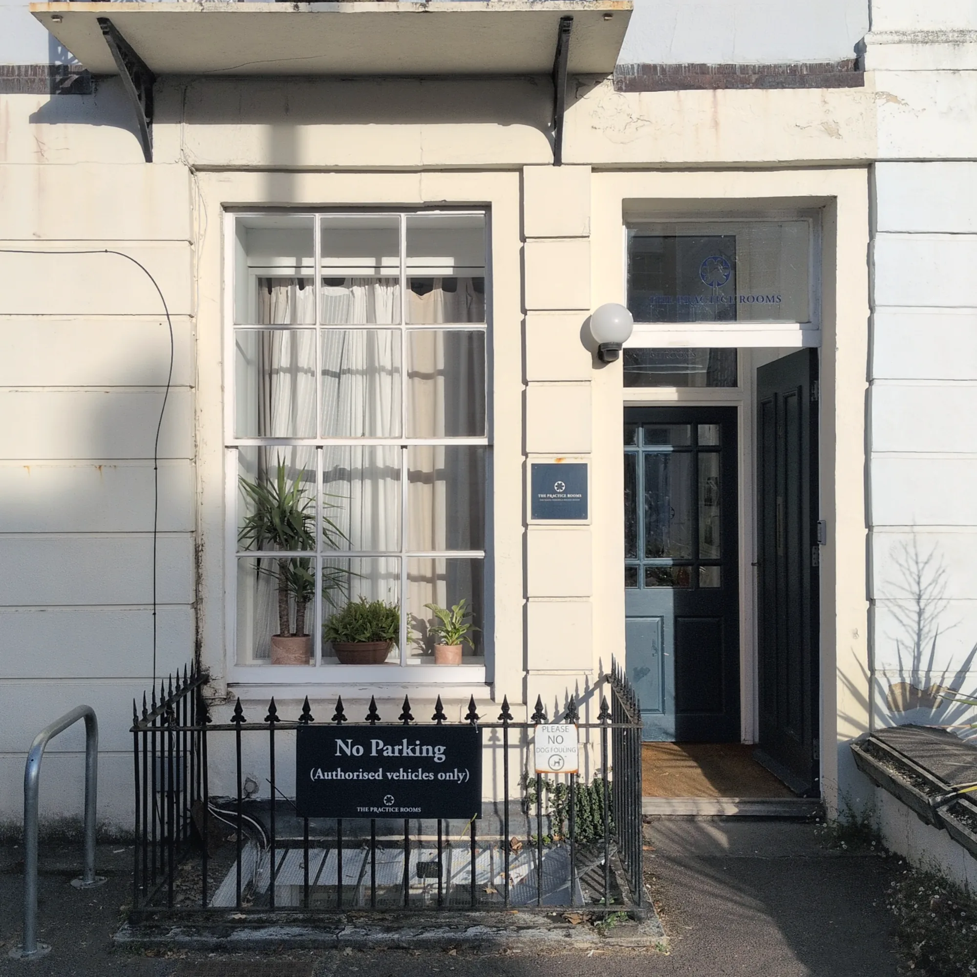 Front door of The Practice Rooms in Clifton, Bristol, standing open: a white Georgian terrace with a sash window, iron railings and a wrought-iron balcony above.